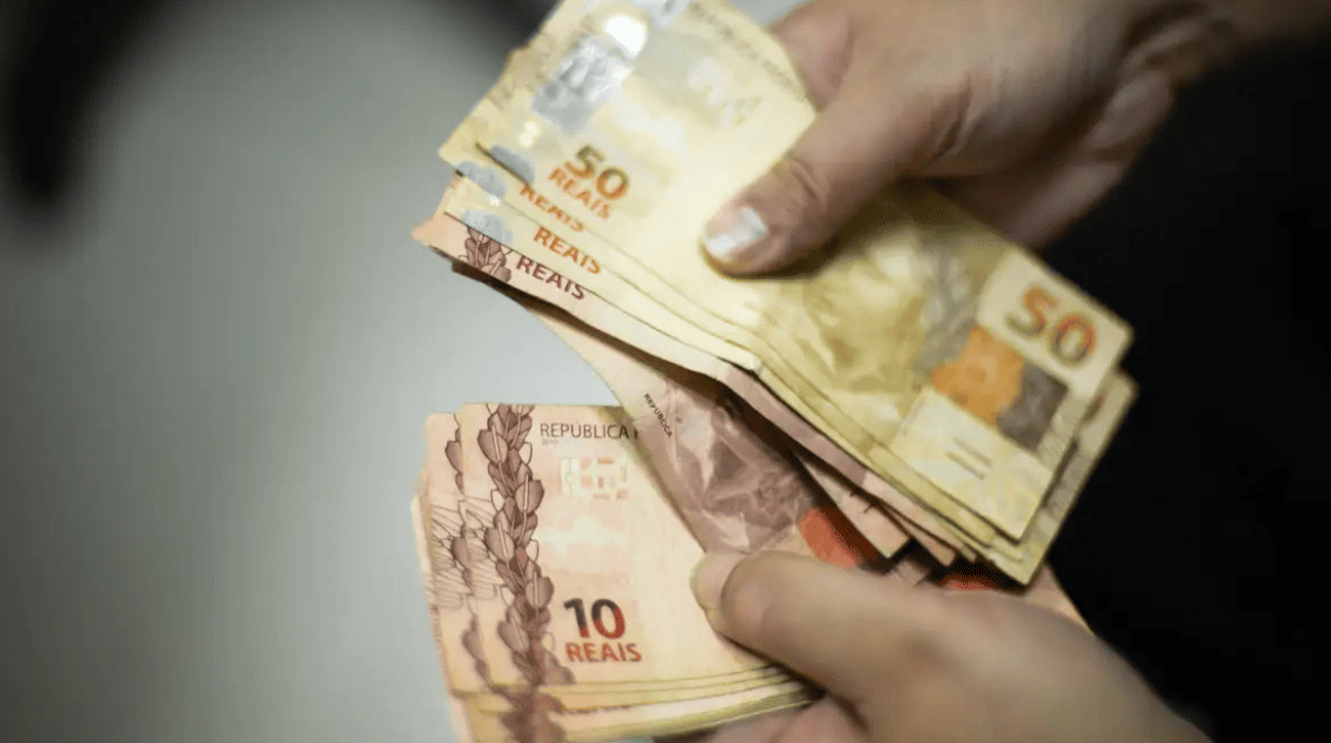 Mão segurando notas de 10 e 50 reais
