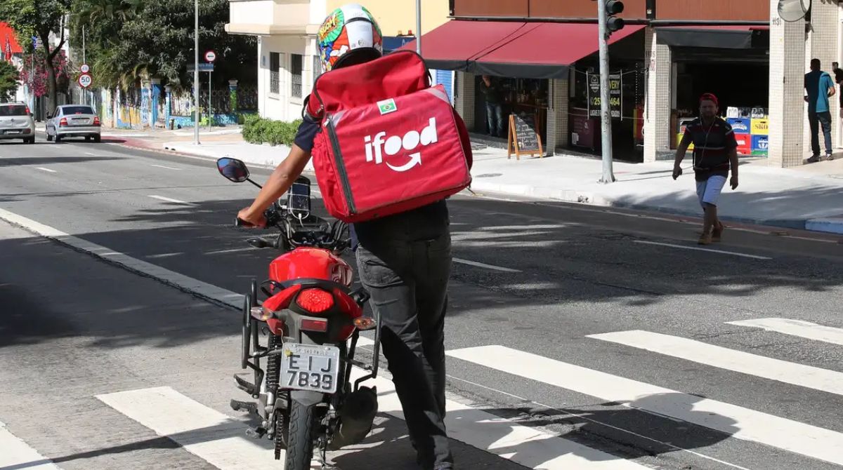 Entregador do Ifood ao lado da moto e com a bag com a logo do aplicativo
